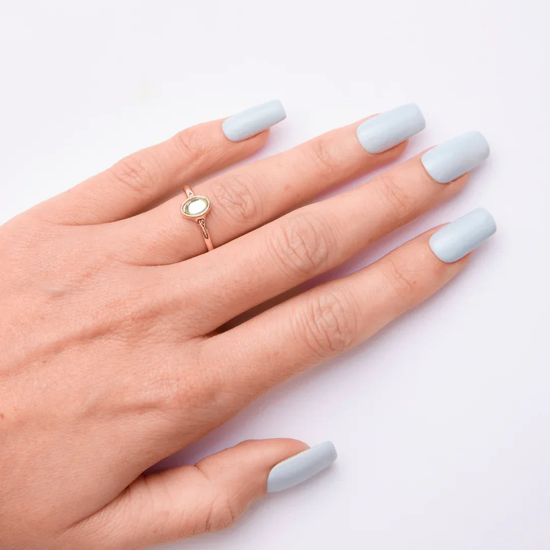 Hand with pastel blue gel nail polish and gold ring on white background