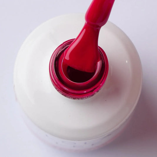 Red gel nail polish bottle with applicator brush, close-up on white background