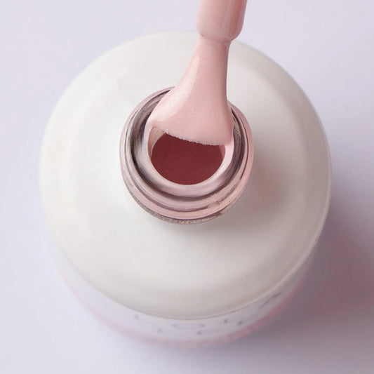 Close-up of a brush with pale pink gel nail polish above an open bottle