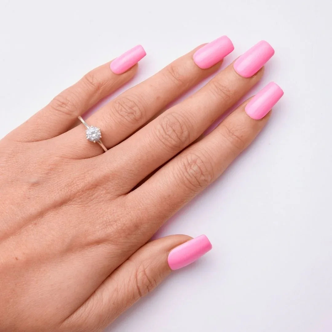 Hand with long pink gel nail polish and solitaire ring on white background