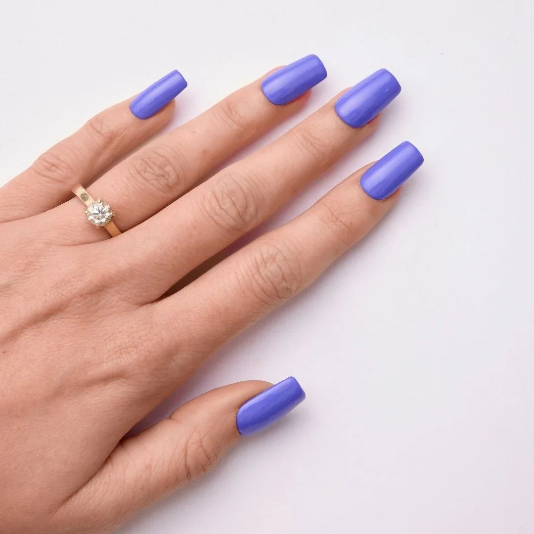 Hand with long square-shaped nails painted purple gel polish and a gold ring on white background