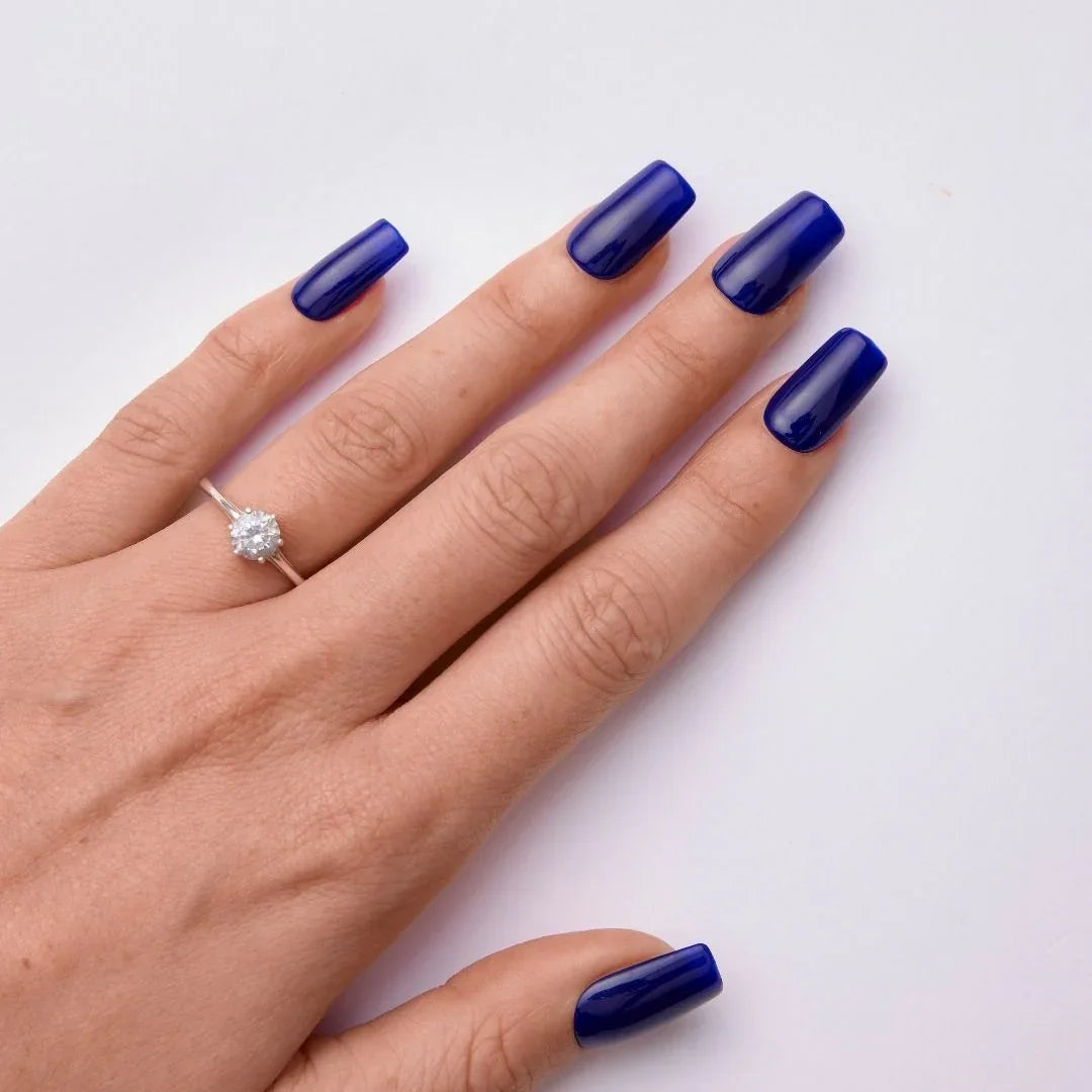 Hand with glossy blue gel nail polish and cubic zirconia ring on white background