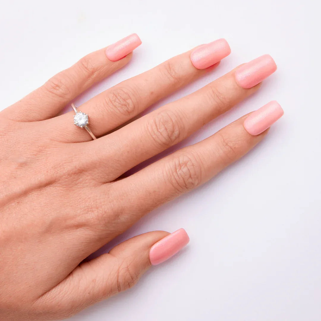 Hand with long light pink gel nail polish and a diamond ring on white background