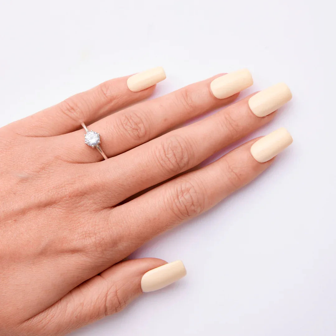Hand with pale yellow gel nail polish and solitaire ring on white background
