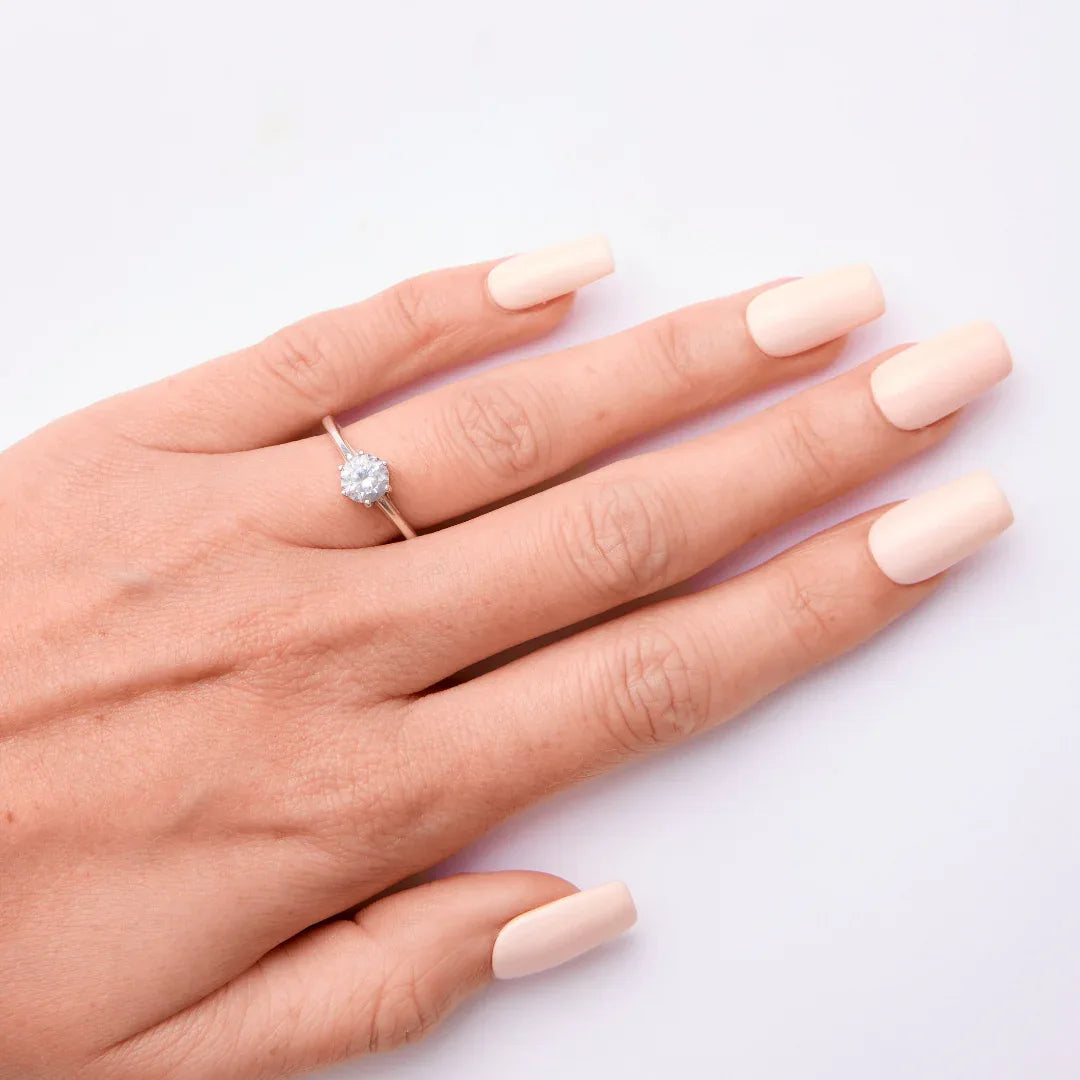 Hand with natural nude gel nail polish and a silver ring on a white background