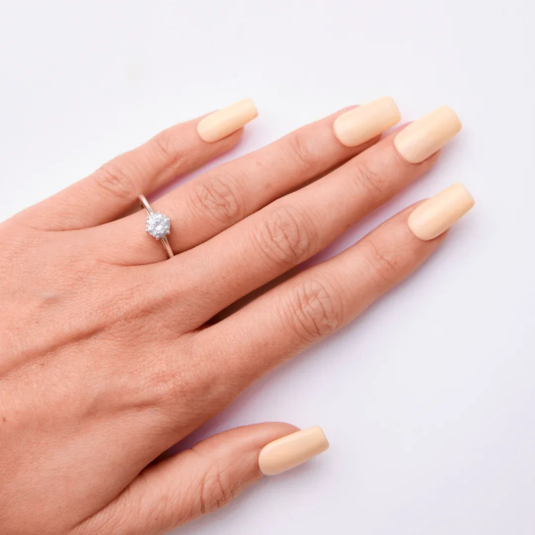 Hand with pastel nude gel nail polish and solitaire ring on white background