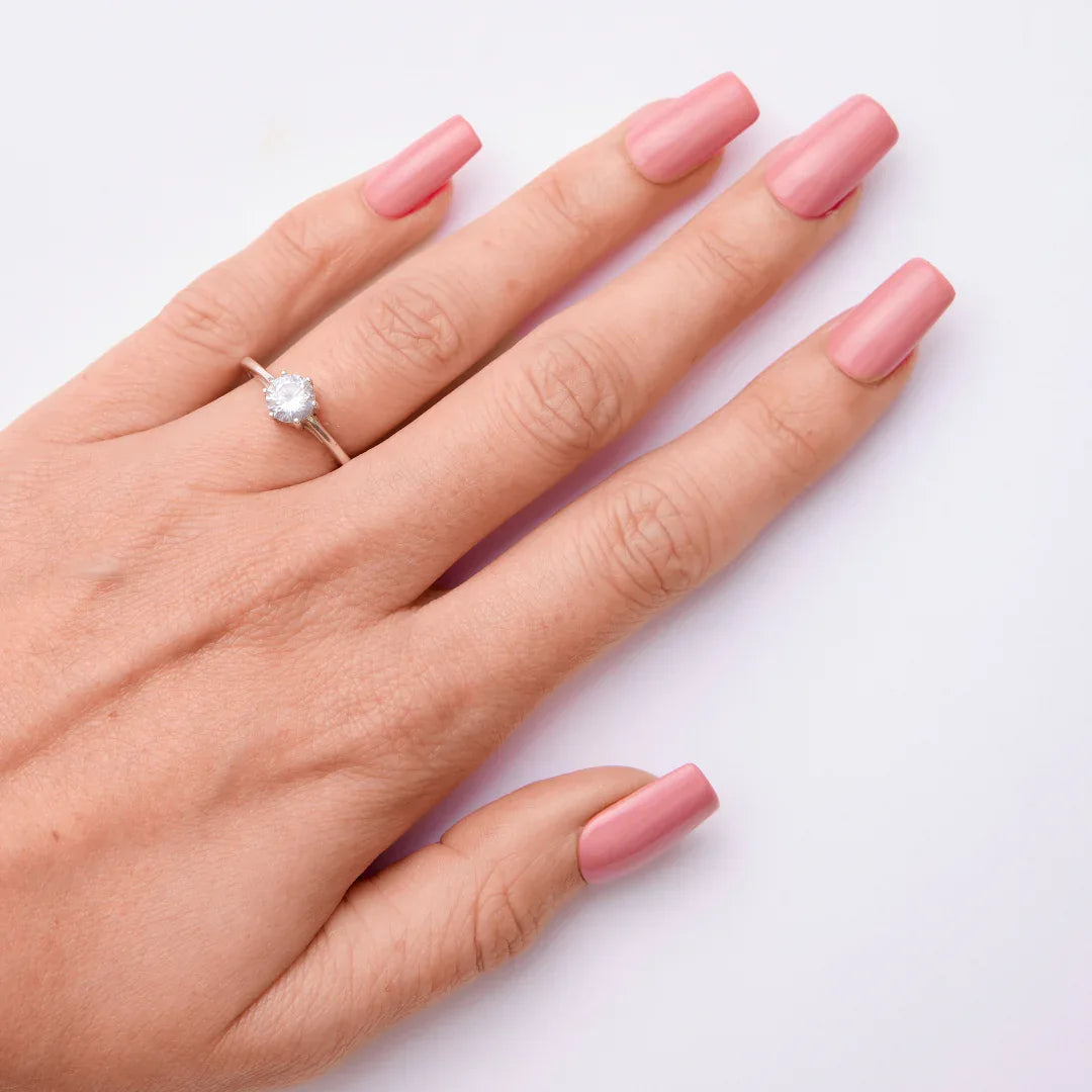 Hand with long square pink gel nail polish and silver ring on white background