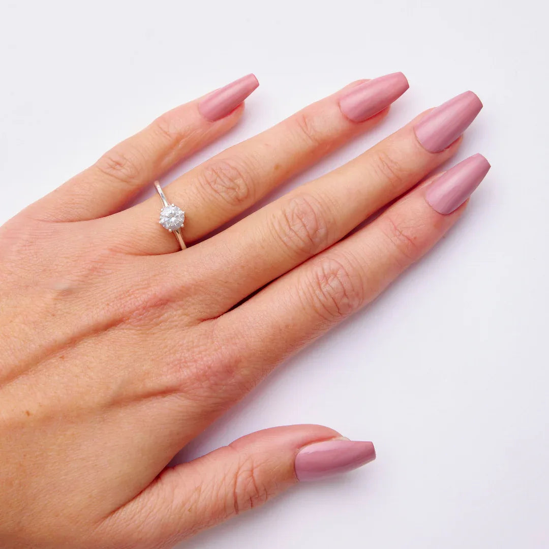 Hand with mauve gel nail polish and engagement ring on a white background