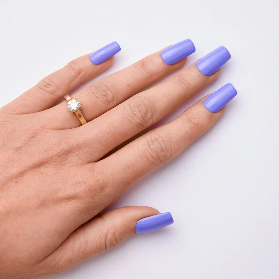 Hand with long square lavender gel nail polish and gold ring on white background