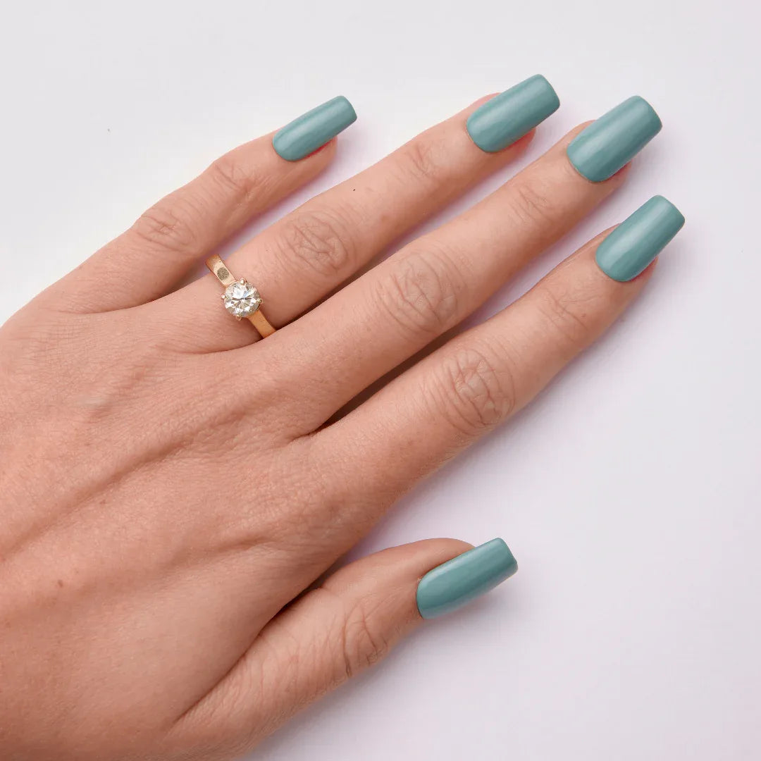 Hand with long teal gel nail polish and gold ring on white background