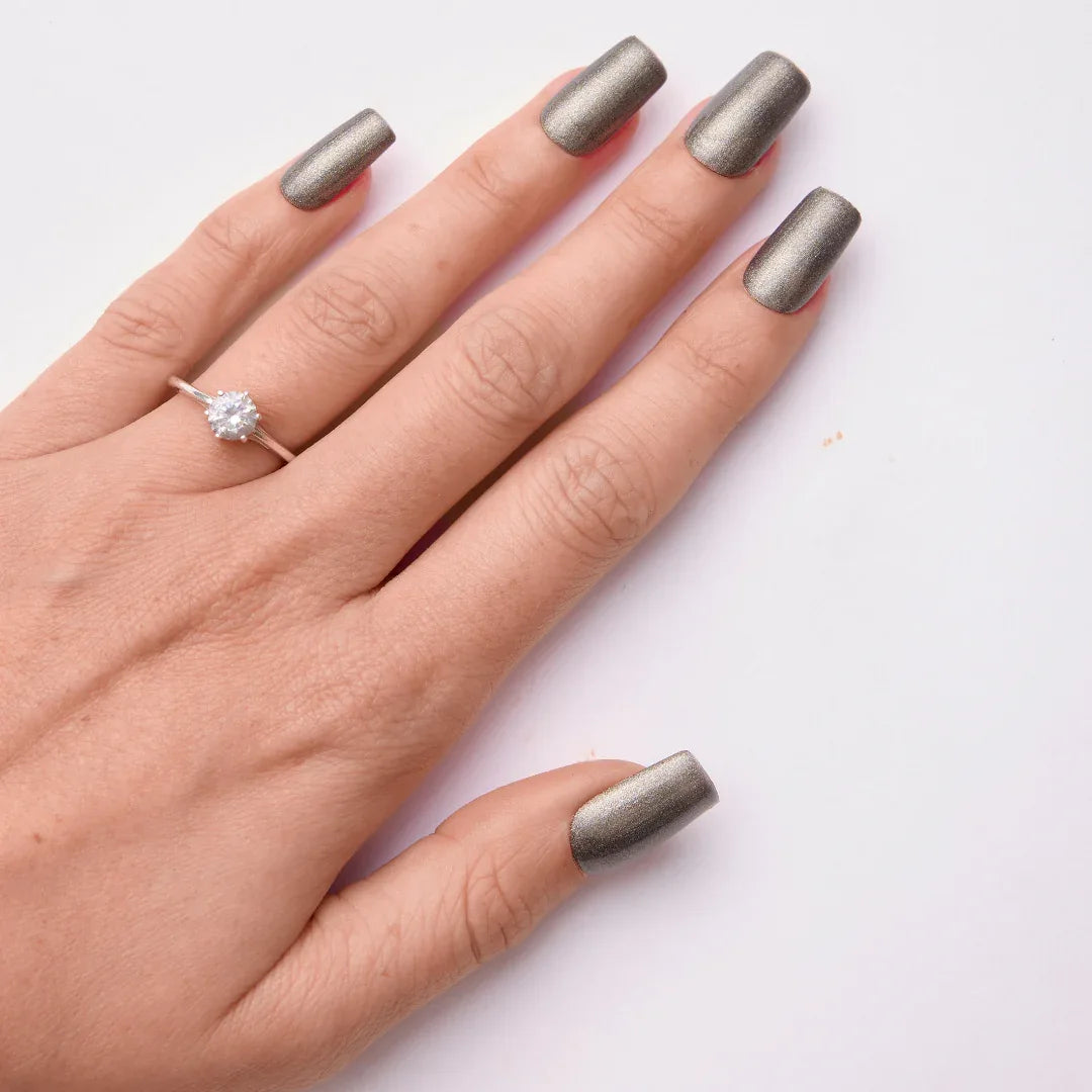 Hand with metallic grey gel nail polish and a silver ring on a white background