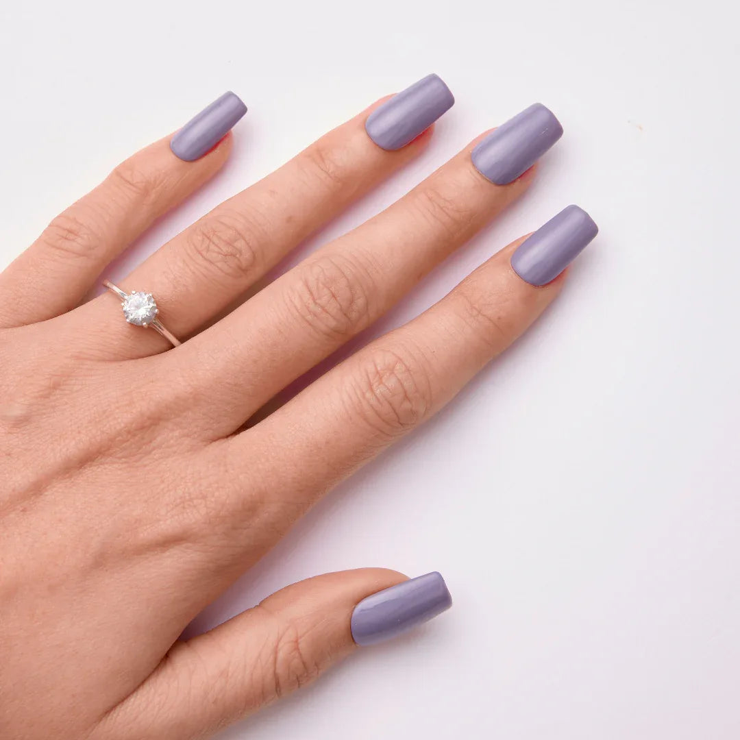 Hand with long square-shaped lavender gel nail polish and a solitaire ring on white background