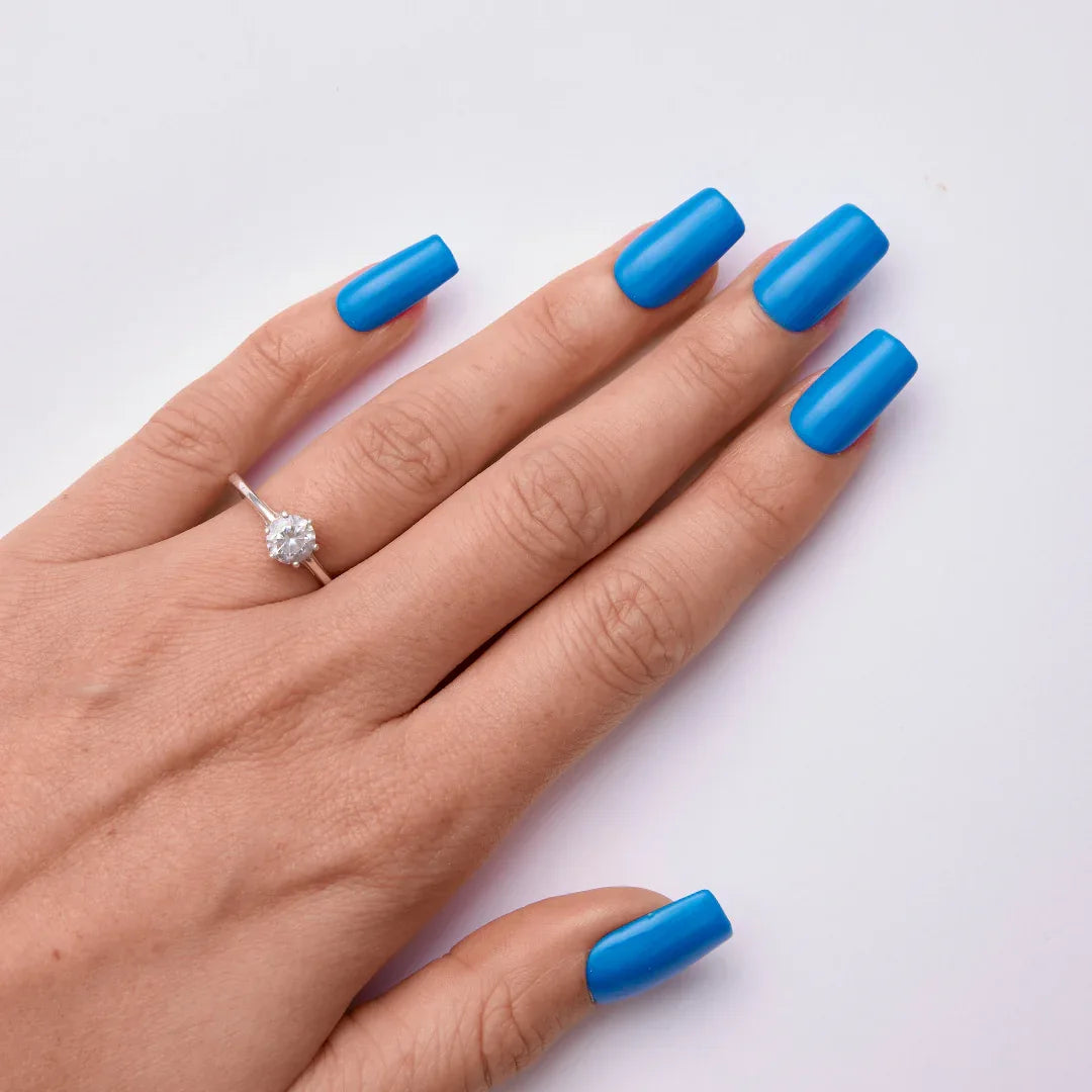 Hand with long square blue gel nails and a solitaire ring on white background