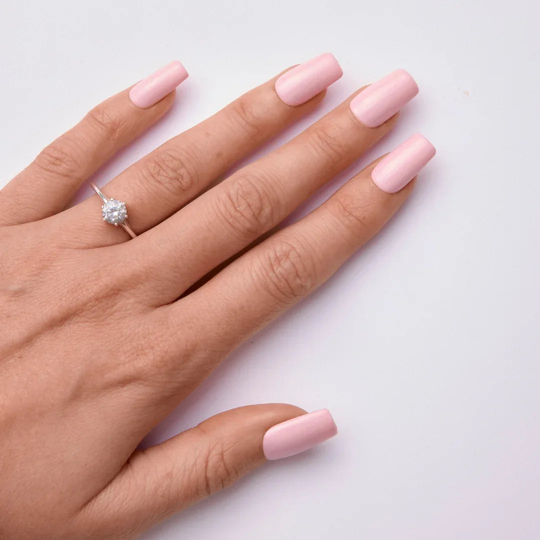 Hand with soft pink gel nail polish and a silver ring on a white background