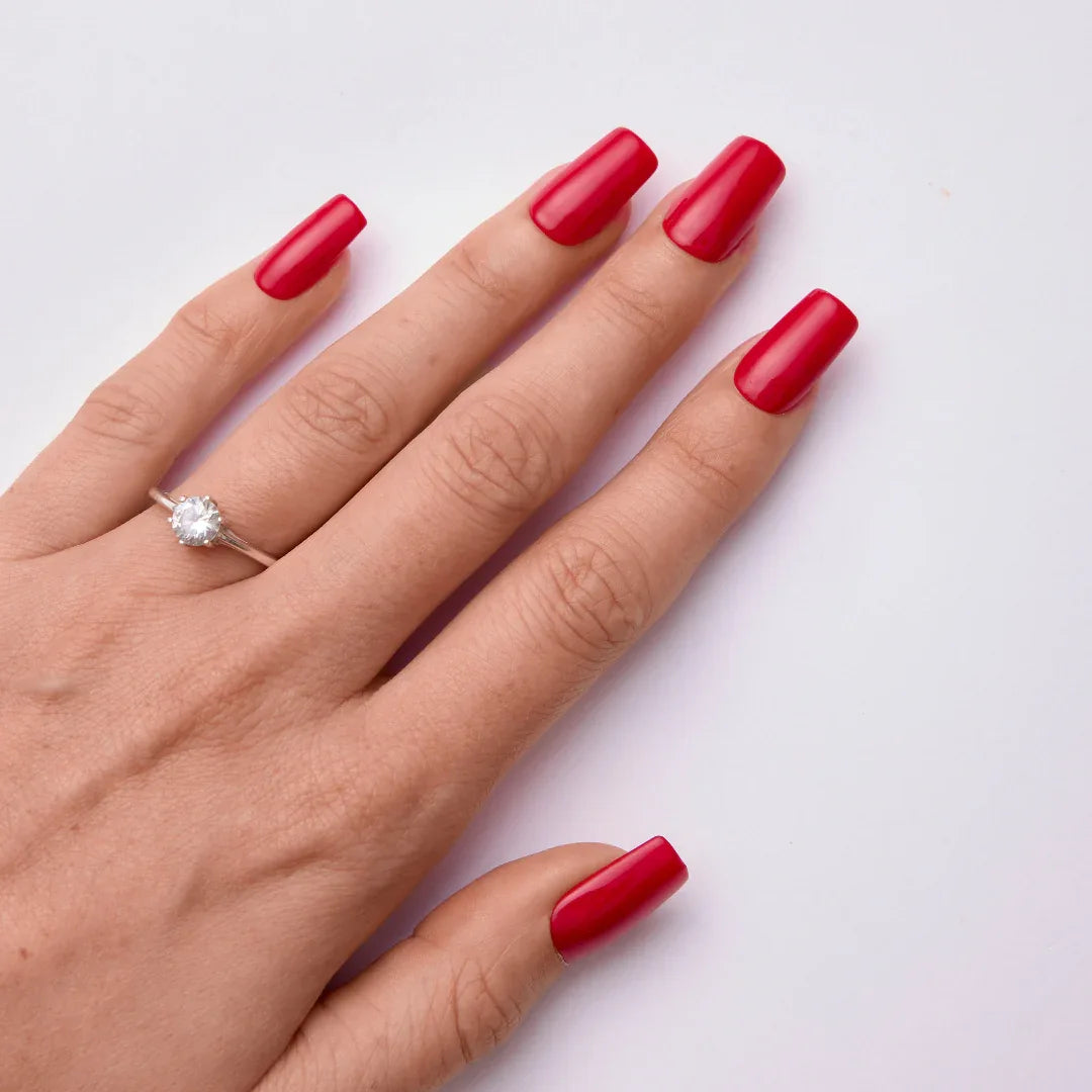Hand with long red gel nail polish manicure and solitaire ring on white background